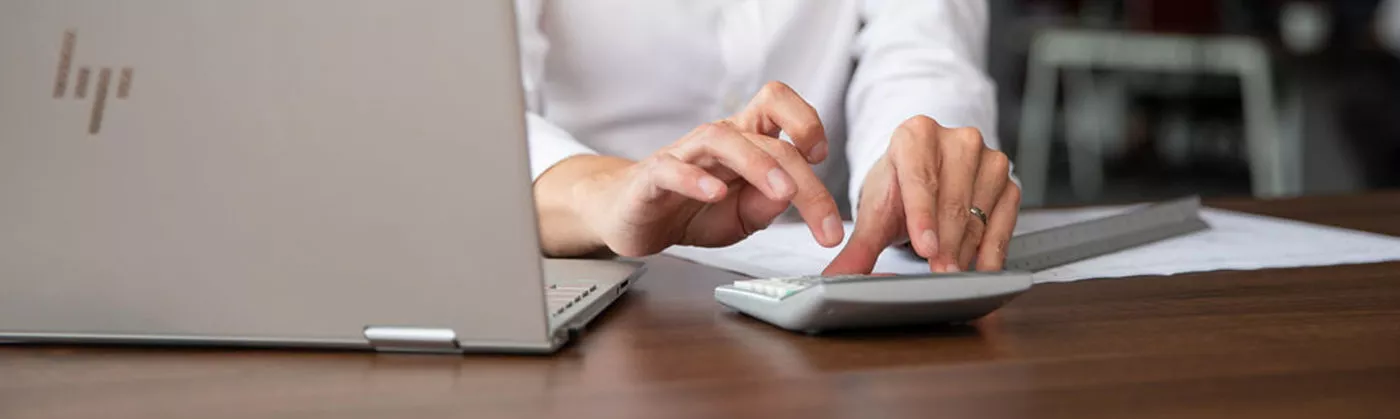 Man inputing calculation in to calculator next to a computer